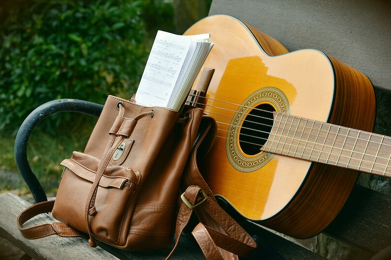 An acoustic guitar next to a bag full of sheet music.