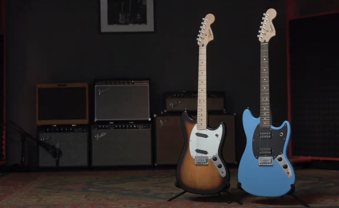 Two Squier Sonic guitars next to each other in front of a bunch of amps