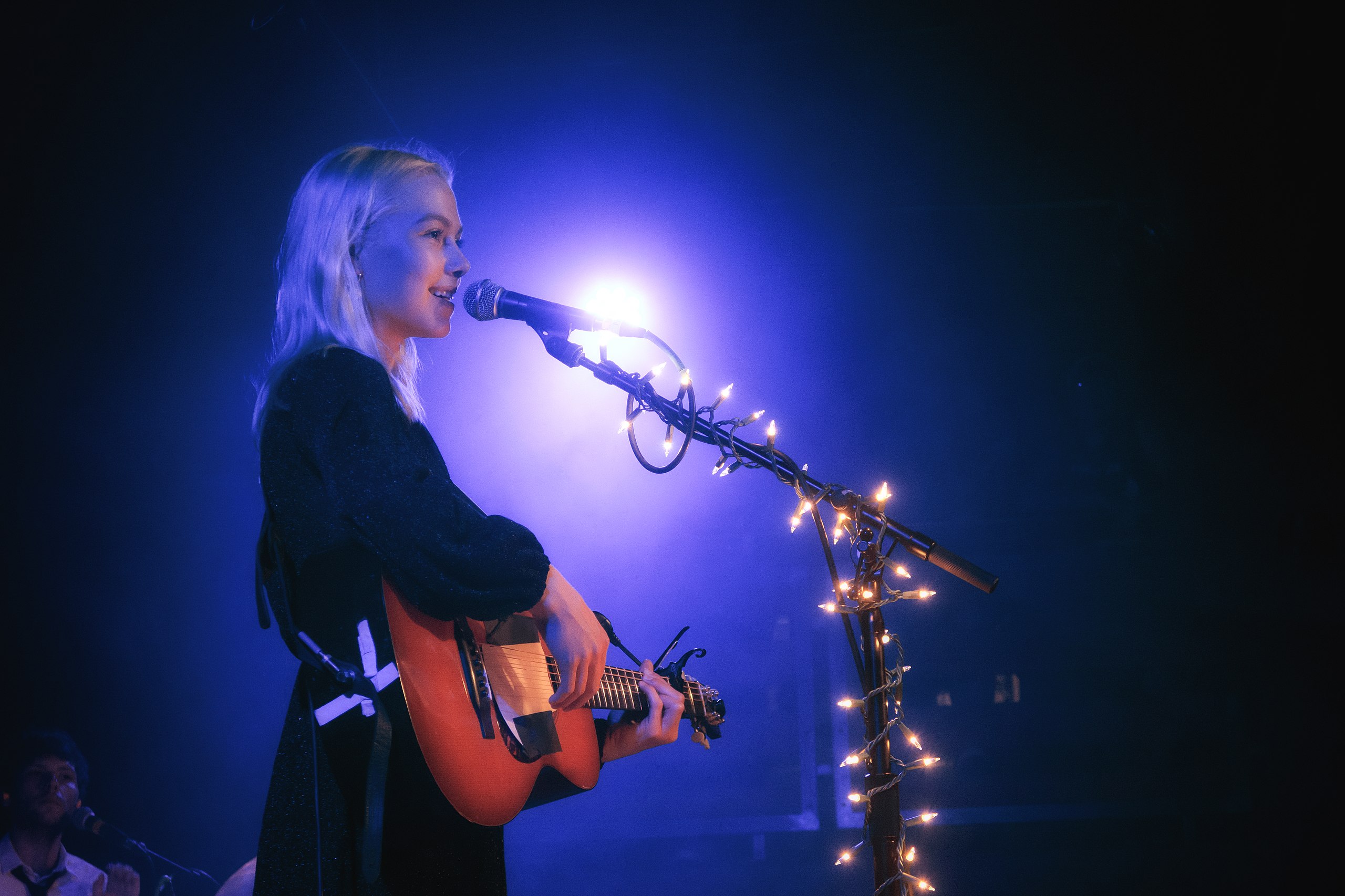 Phoebe Bridgers playing an acoustic guitar live.